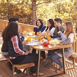 Man barbecues for friends at a table, on a deck in a forest